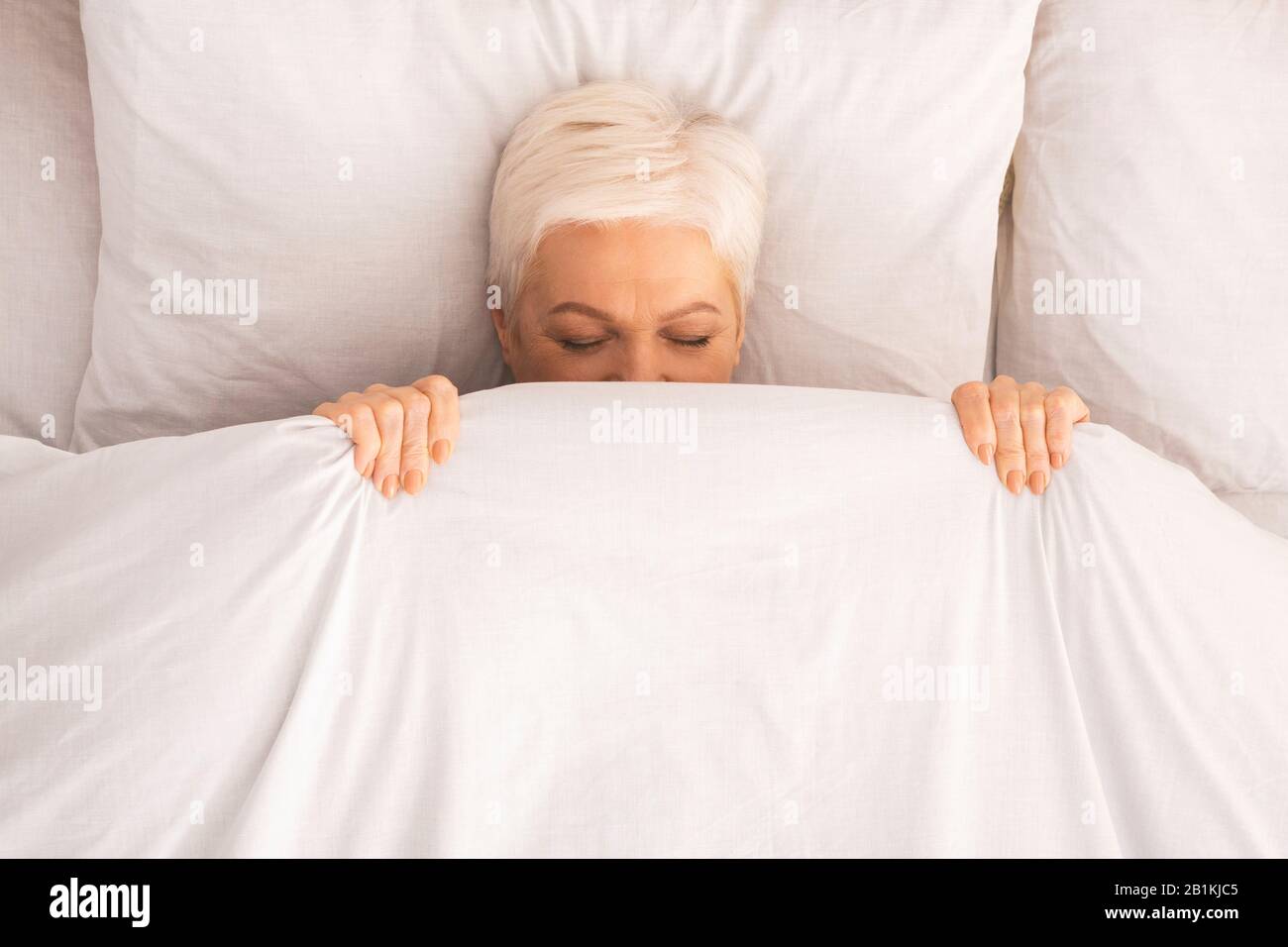 Retired lady lying in bed and playing hide-and-seek Stock Photo