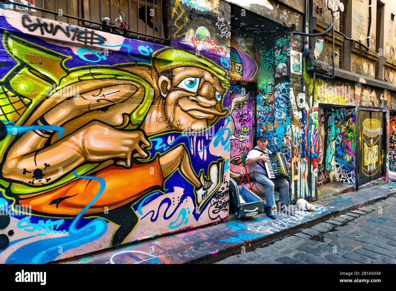 Elderly man playing piano accordian with dog, busking in graffiti filled cobbled stone alleyway, Hosier Street, Melbourne Lanes, Melbourne, Victoria, Stock Photo