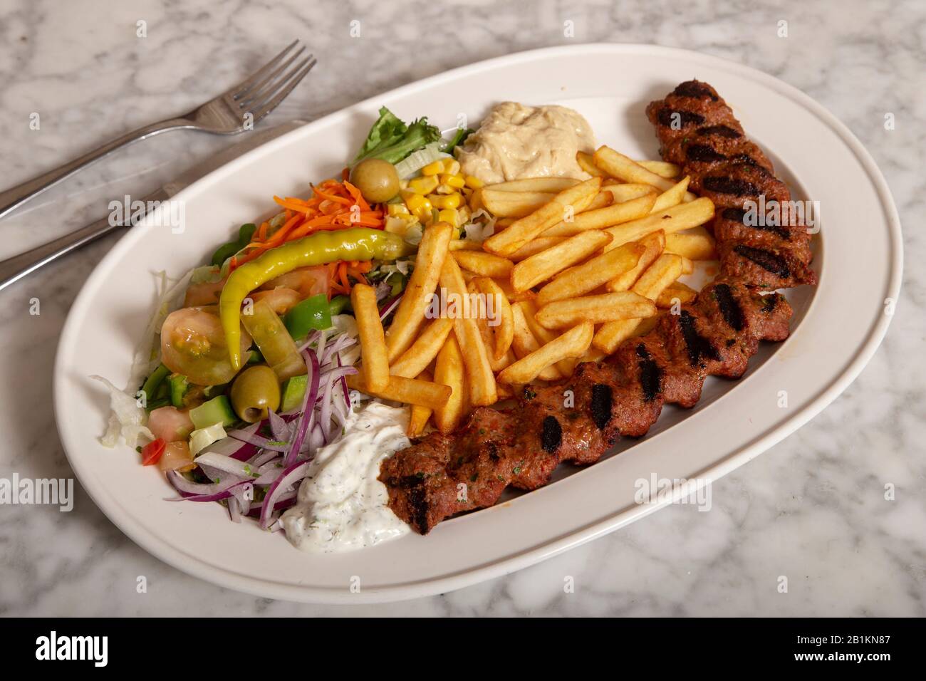 Turkish food dish. Adana kebab with hummus chips and salad. Stock Photo