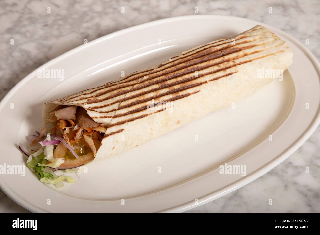 Durum kebab in hard bread served on plate on white marble table. Stock Photo
