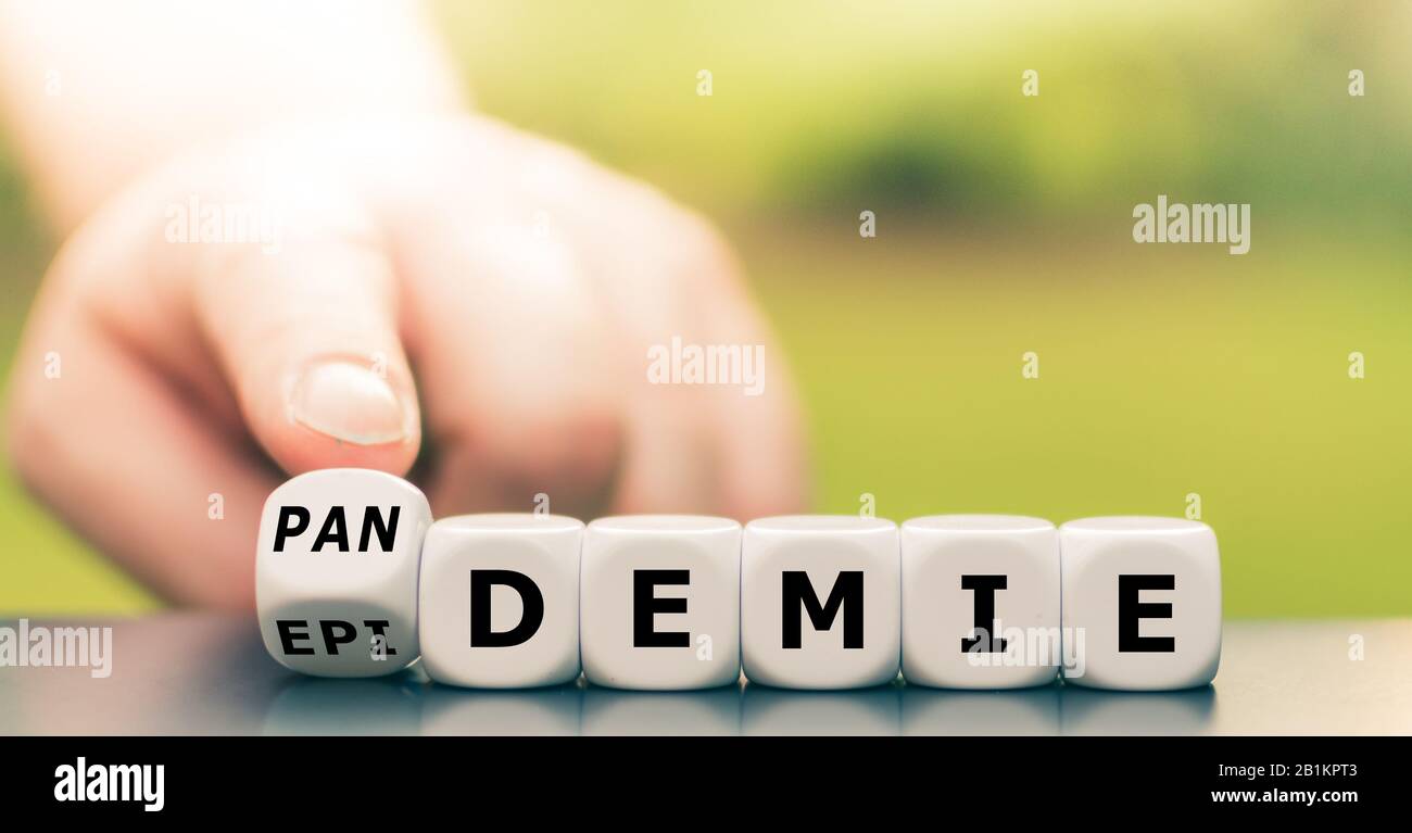 Hand turns dice and changes the German word 'Epidemie' ('epidemic') to 'Pandemie' ('pandemic'). Stock Photo