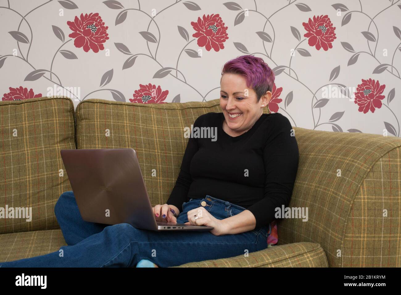 A woman sat on her sofa on her laptop computer looking excited Stock Photo
