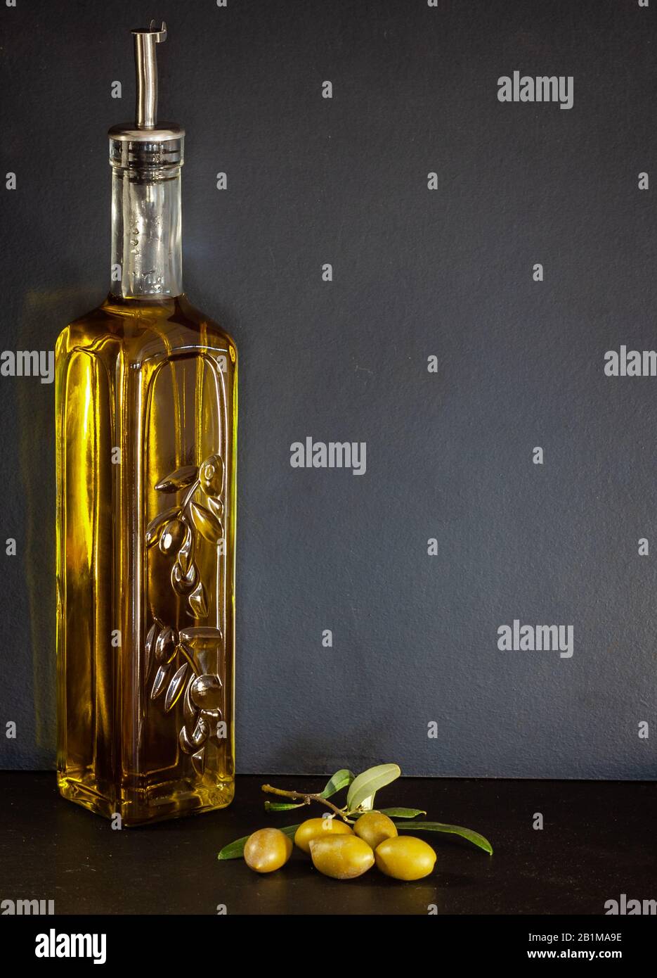 Glass bottle of olive oil with olives and an olive branch with leaves ...