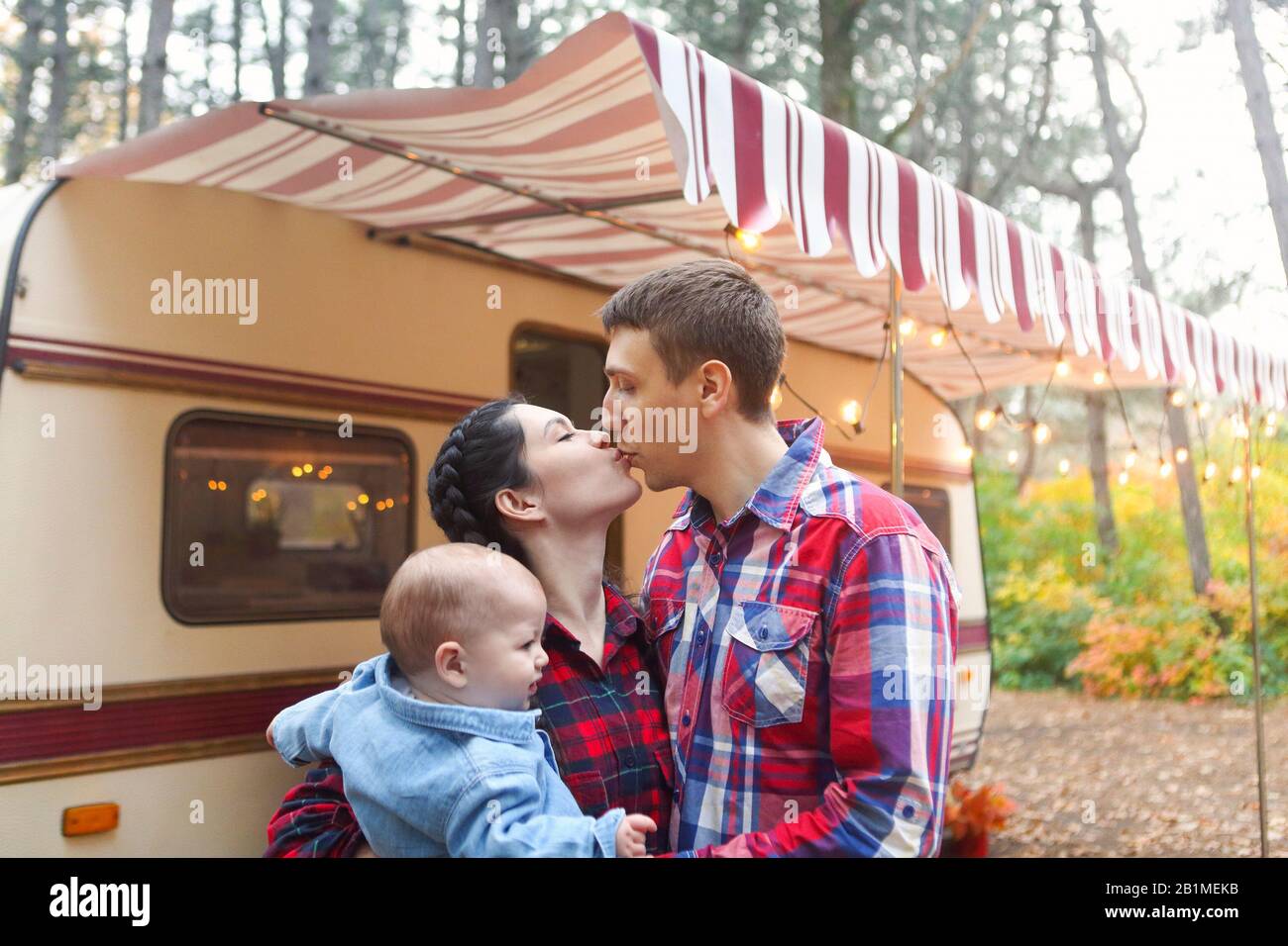 Portrait of a young smiling family while hugging near house on wheels outdoors Stock Photo