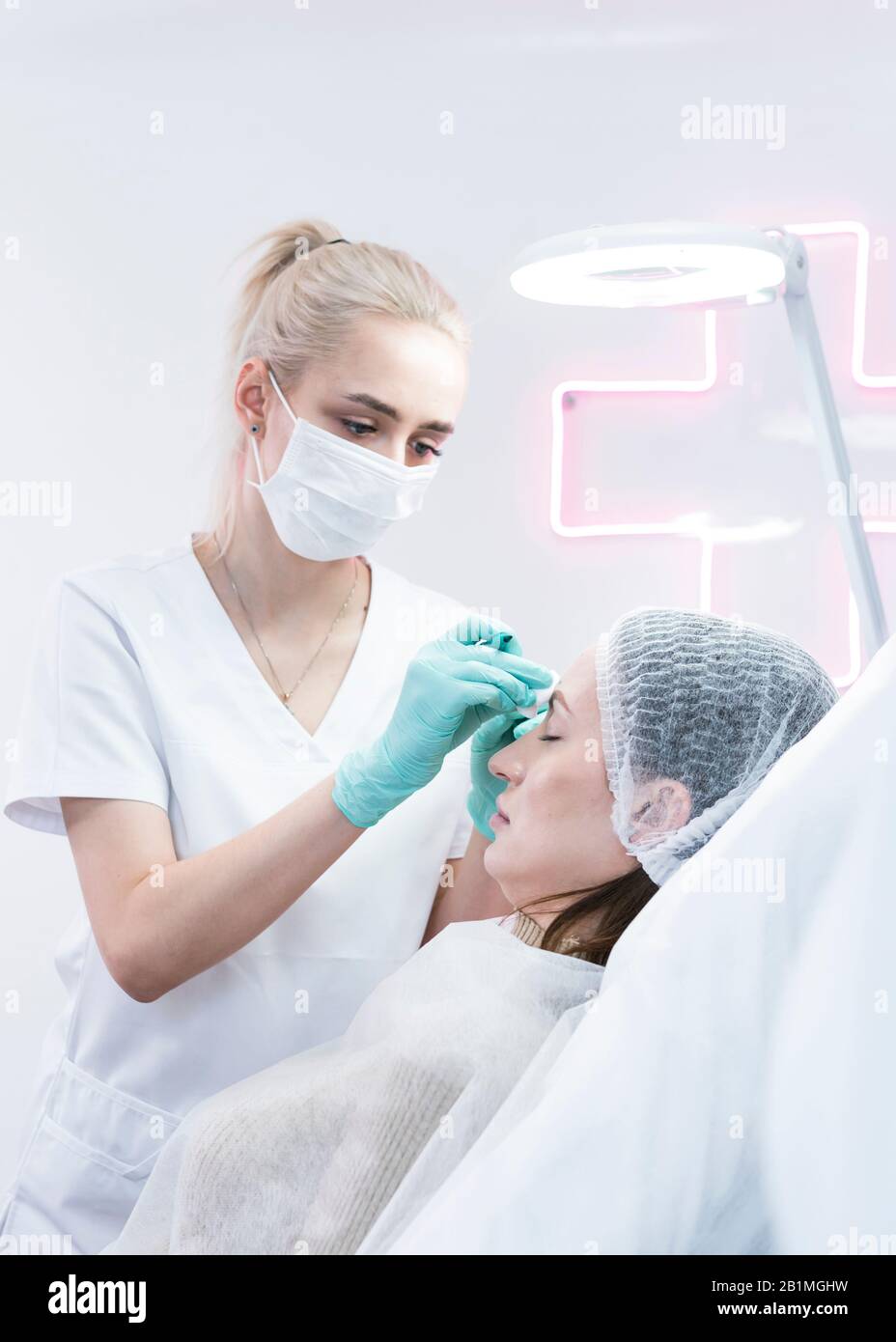 The young beautician doctor preparing to making injection in female forehead. The doctor cosmetologist makes anti-aging treatment and face lift proced Stock Photo