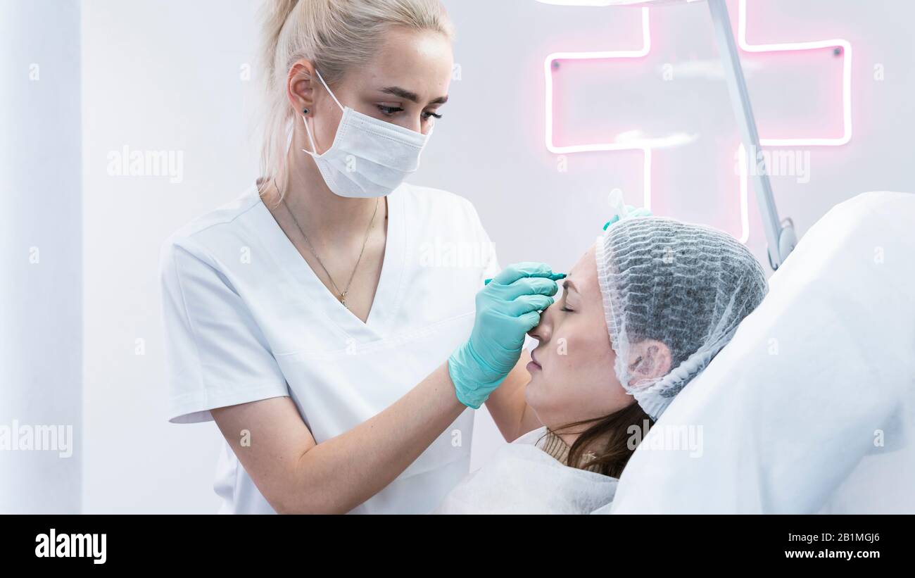 The young beautician doctor preparing to making injection in female forehead. The doctor cosmetologist makes anti-aging treatment and face lift proced Stock Photo