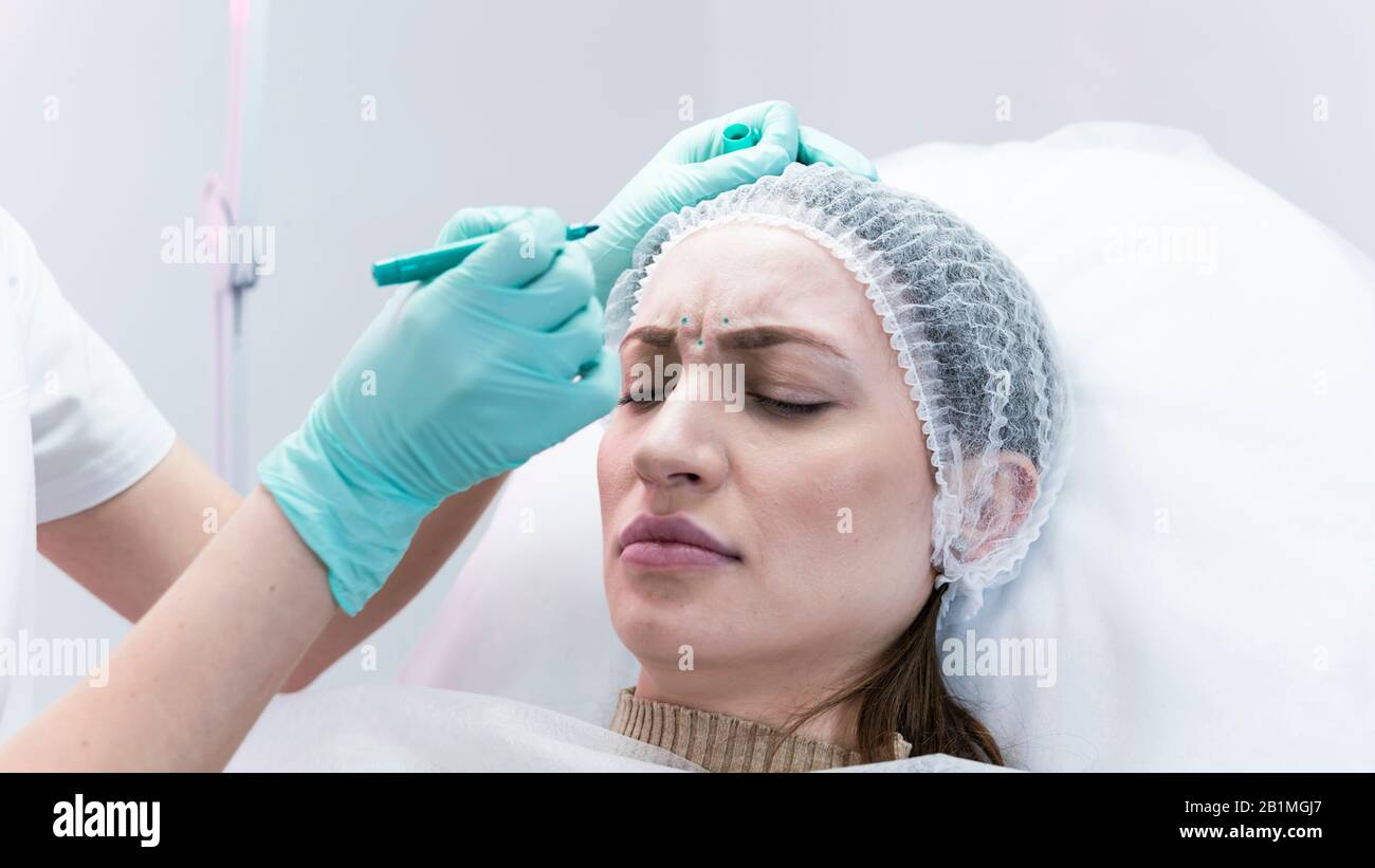 The young beautician doctor preparing to making injection in female forehead. The doctor cosmetologist makes anti-aging treatment and face lift proced Stock Photo