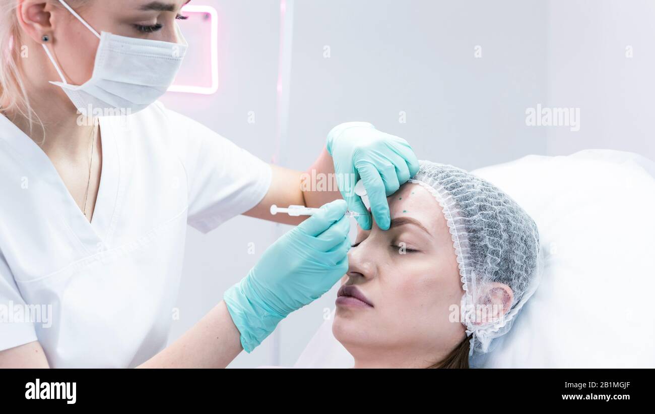 The young beautician doctor preparing to making injection in female forehead. The doctor cosmetologist makes anti-aging treatment and face lift proced Stock Photo