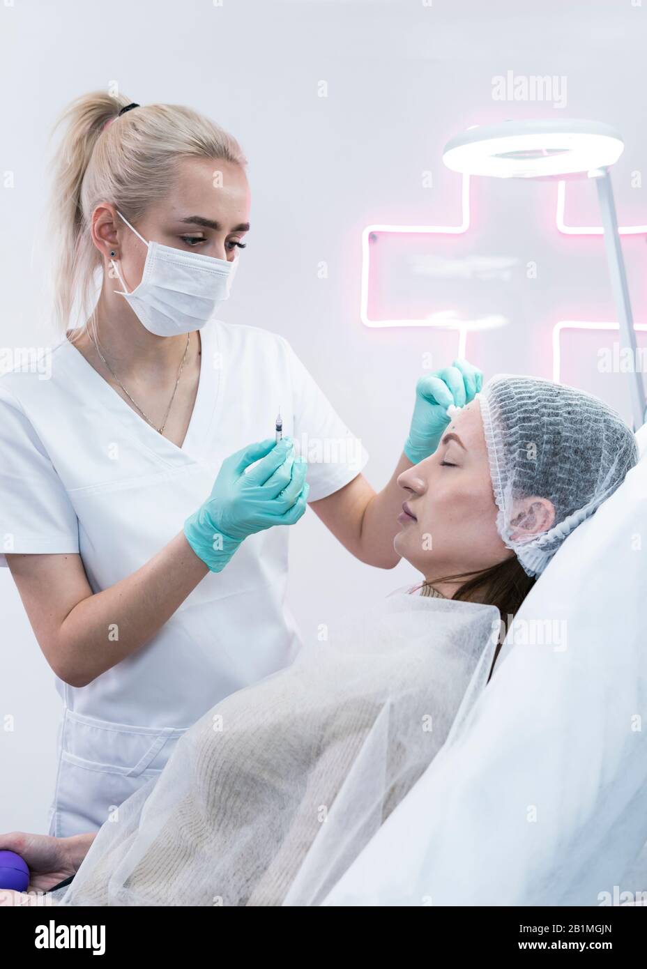 The young beautician doctor preparing to making injection in female forehead. The doctor cosmetologist makes anti-aging treatment and face lift proced Stock Photo