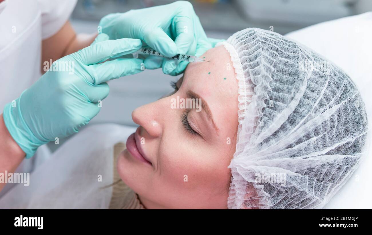 The young beautician doctor preparing to making injection in female forehead. The doctor cosmetologist makes anti-aging treatment and face lift proced Stock Photo