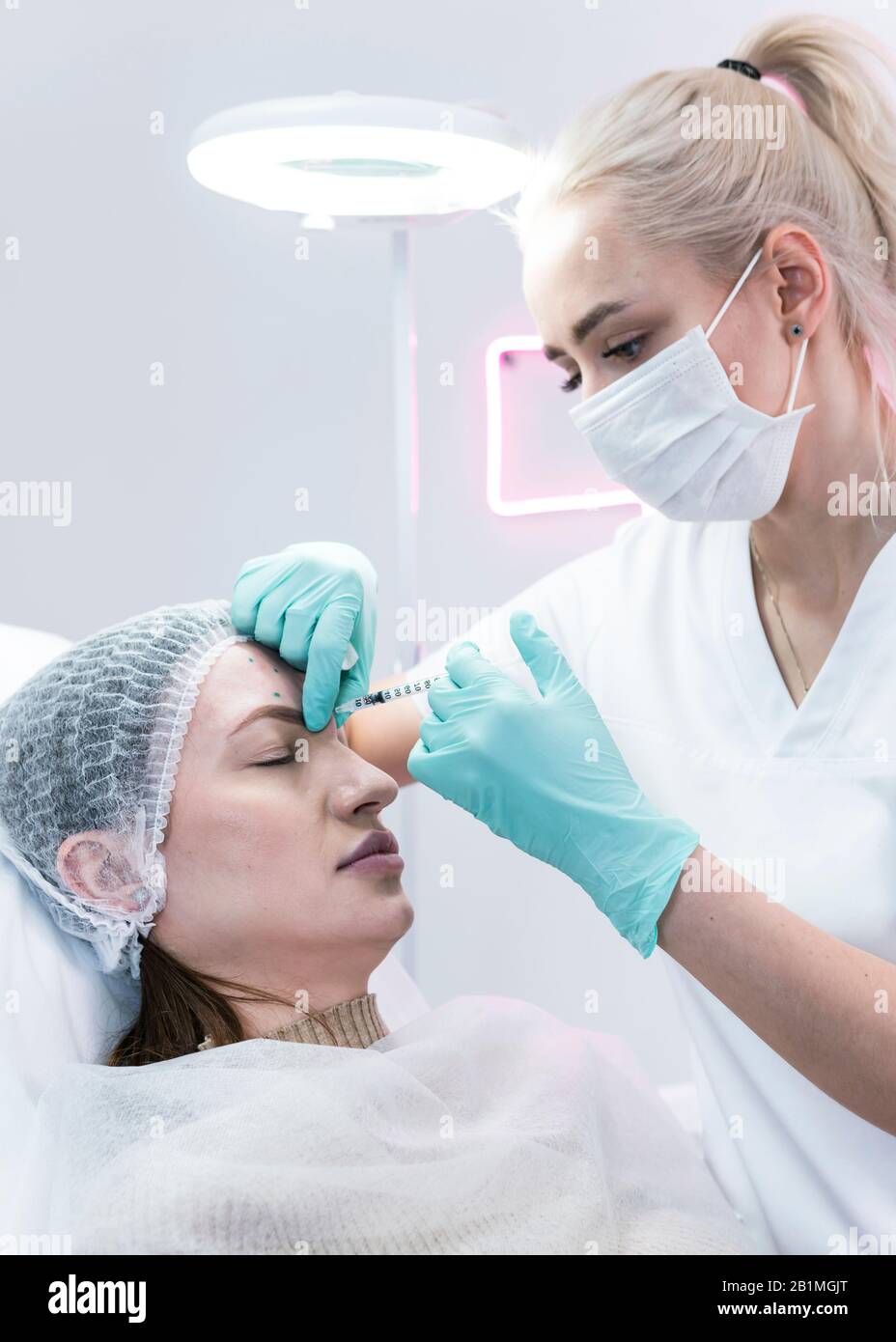 The young beautician doctor preparing to making injection in female forehead. The doctor cosmetologist makes anti-aging treatment and face lift proced Stock Photo