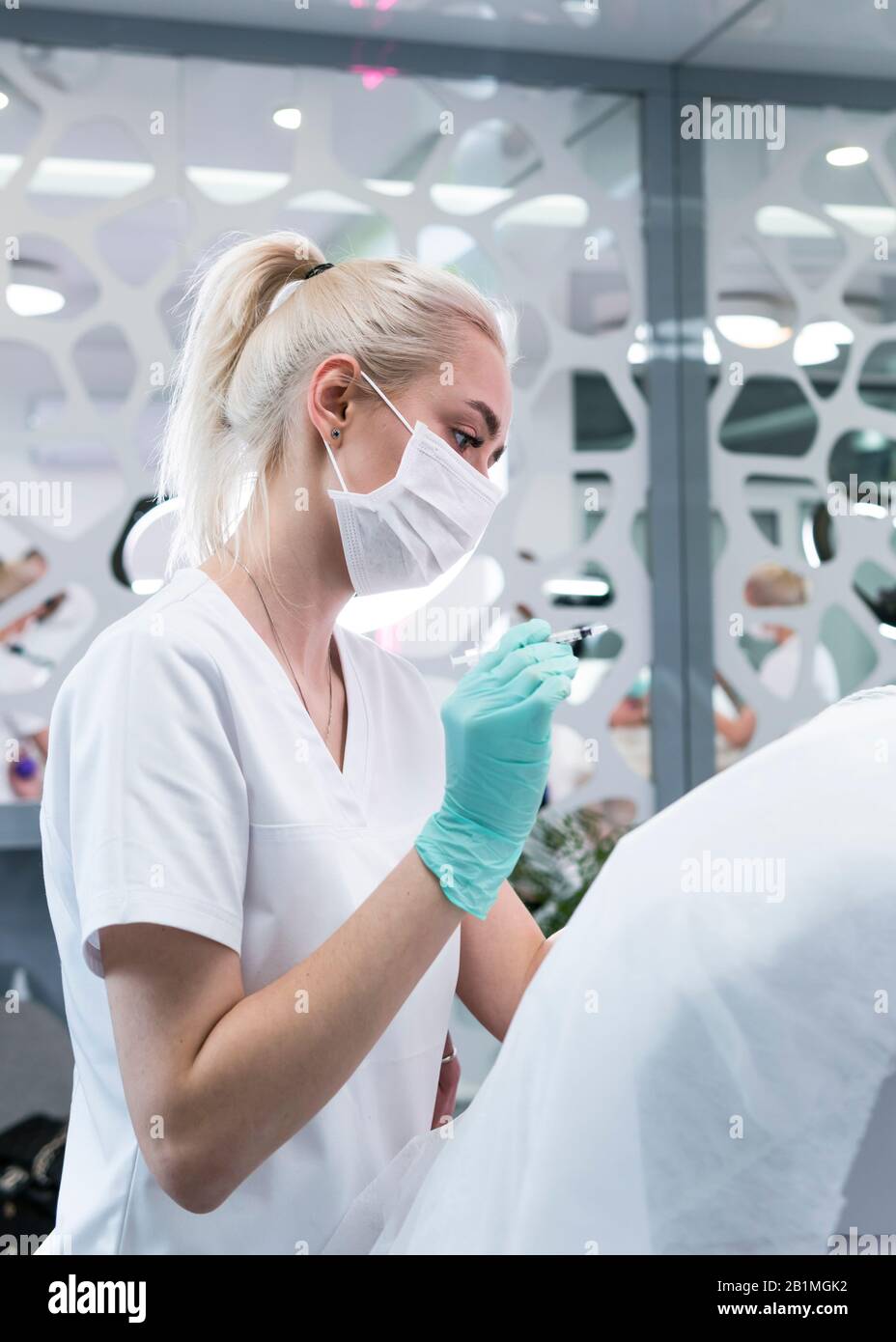 The young beautician doctor preparing to making injection in female forehead. The doctor cosmetologist makes anti-aging treatment and face lift proced Stock Photo