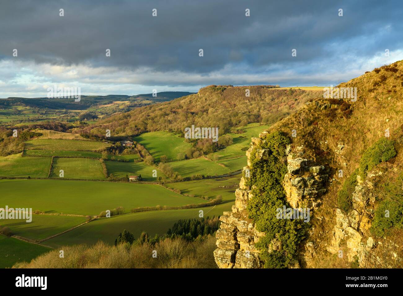 Beautiful scenic long-distance view of sunlit Sutton Bank escarpment, Roulston Scar cliff face, farmland & dark sky - North Yorkshire, England, UK. Stock Photo