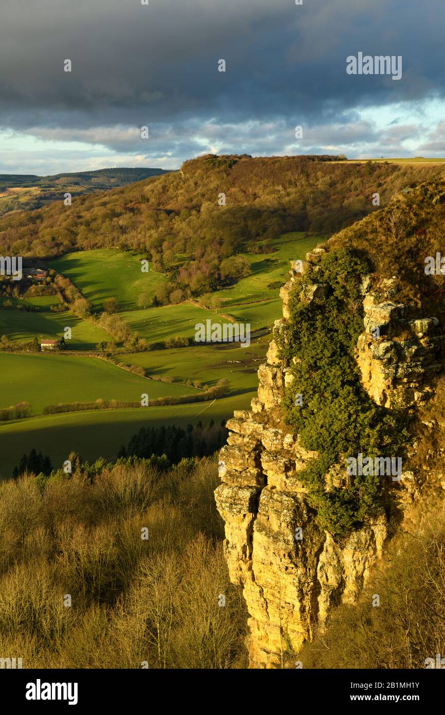 Beautiful scenic long-distance view of sunlit Sutton Bank escarpment, Roulston Scar cliff face, farmland & dark sky - North Yorkshire, England, UK. Stock Photo