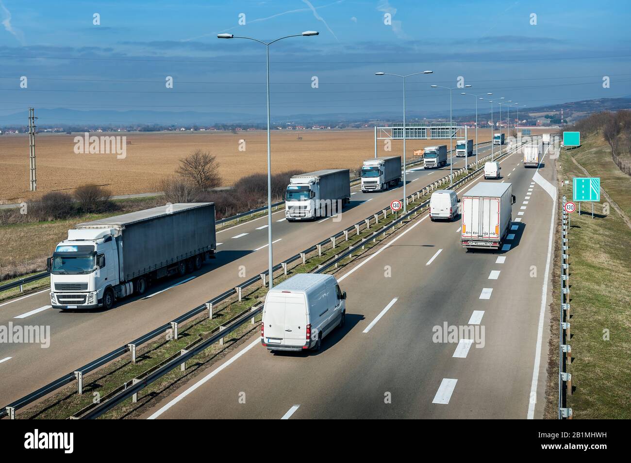 Highway transportation with a convoy of white Lorry trucks passing trucks and vans with a beautiful sunset sky Stock Photo