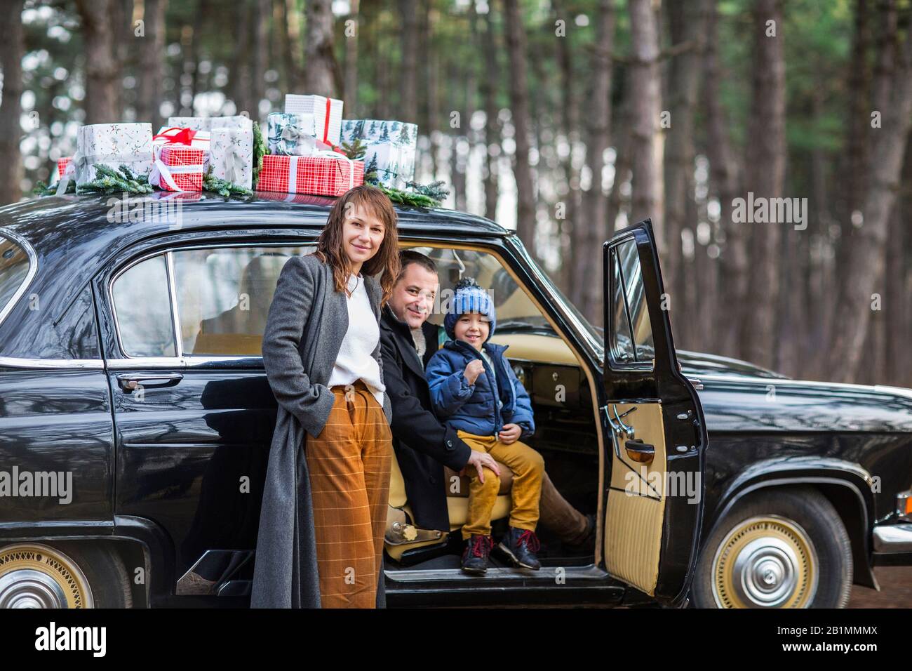 Smiling Adult Man And Woman With Boy In Warm Clothes Standing At Vintage Car With Christmas Presents Stock Photo Alamy