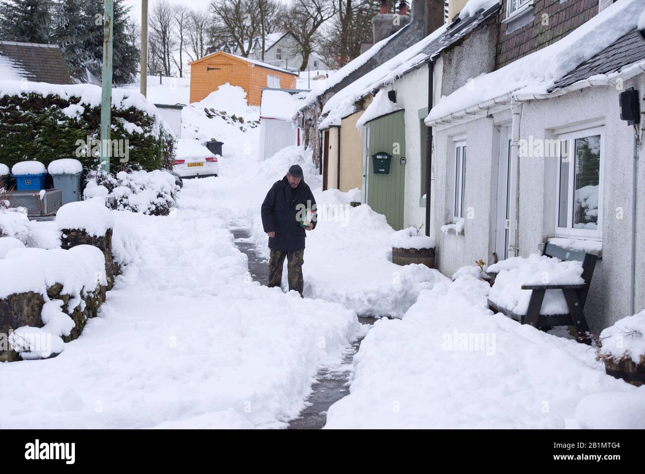 A man walks down a snow covered street in the village of Leadhills, South Lanarkshire, Scotland. Stock Photo