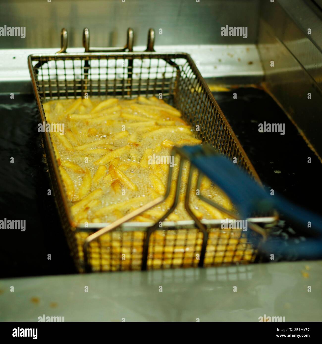 crispy french fries in a deep fat fryer with steel net basket Stock