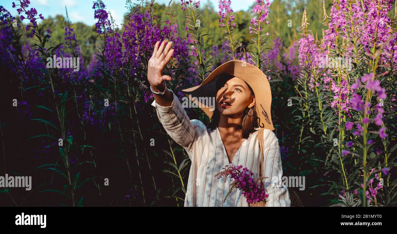 Beautiful woman in a big hat enjoing the sun on a field with flowers. Summer lifestyle. Outdoor Stock Photo