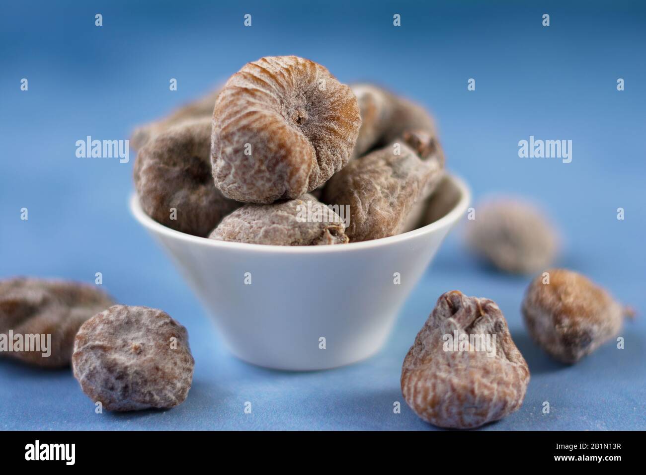 Sun-dried figs besprinkled with powdered sugar, in a white bowl. A few blurry figs are scattered around the bowl. Selective focus. Stock Photo