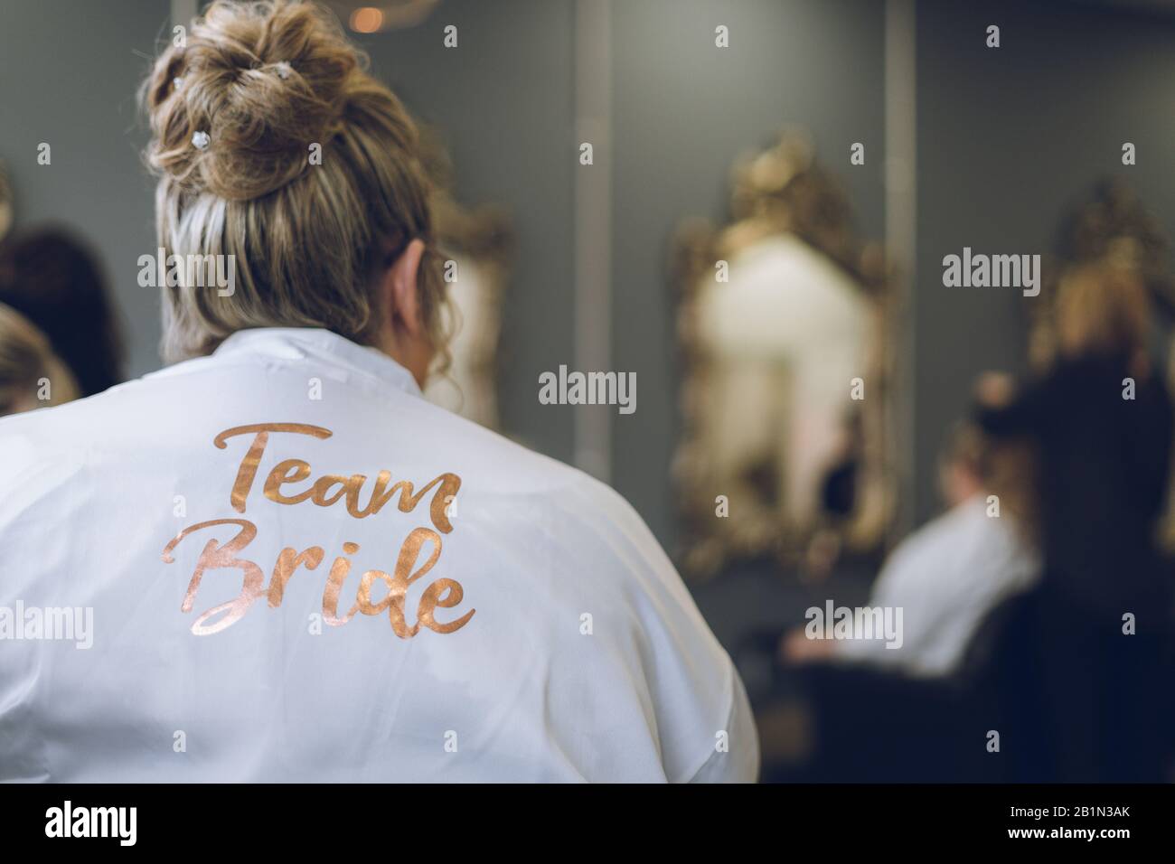 a young woman in a hair salon wearing a dressing gown with the words team bride Stock Photo