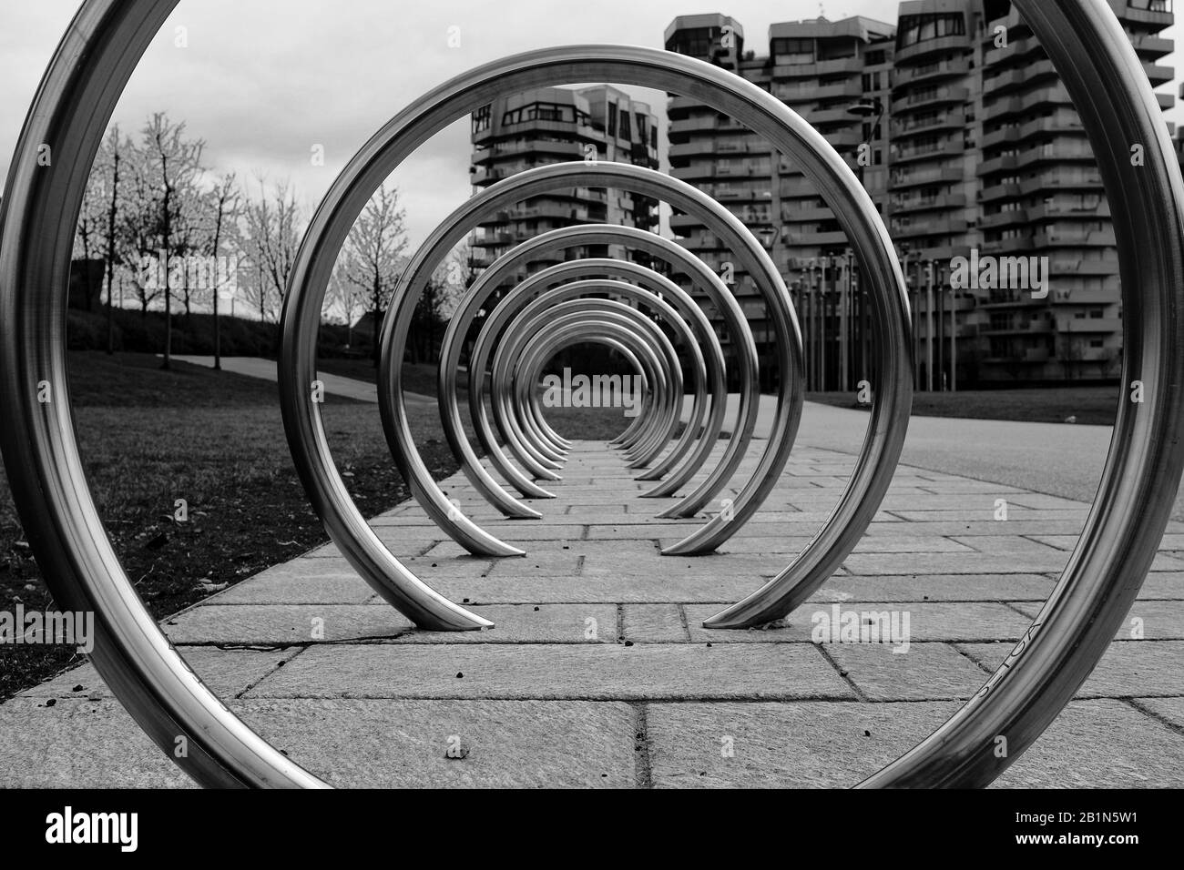 Bicycle inox ring rack in the city park of Citylife, Milan, Italy, with residential buildings and trees in the background Stock Photo