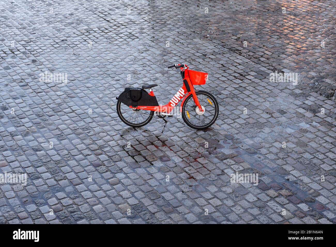 PARIS, FRANCE - FEBRUARY 26, 2020:  JUMP red dockless electric bike acquired by Uber parked ditched right in the middle of a wet cobblestoned place. Stock Photo