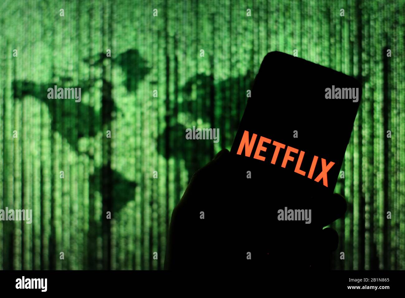 Netflix logo seen displayed on smart phone screen with Matrix-like world map visible blurred in the background Stock Photo