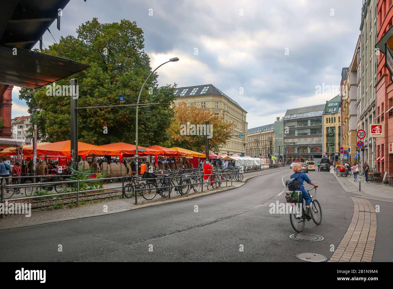 A woman rides a bicycles down a busy street past the Hackescher Markt square in the Mitte district of Berlin Germany Stock Photo