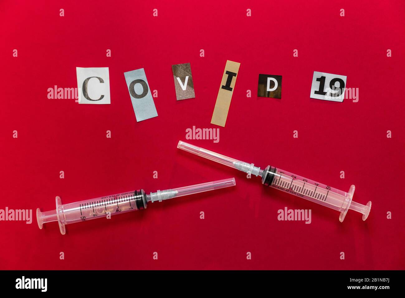Two medical syringes and COVID-19 text made  of paper-cut letters on red background. Copy space. Chinese coronavirus outbreak Stock Photo