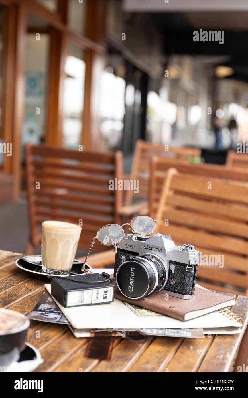 Analogue Canon camera on wooden outdoor cafe table with latte, book and negatives under shop verandah in Daylesford. Stock Photo