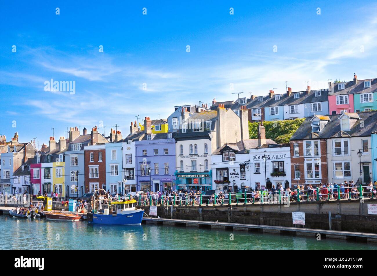 Tourists on the quay at the Old Harbour walking past the colourful shops, restaurants and properties on Trinity Road, Weymouth, Dorset, England, UK Stock Photo