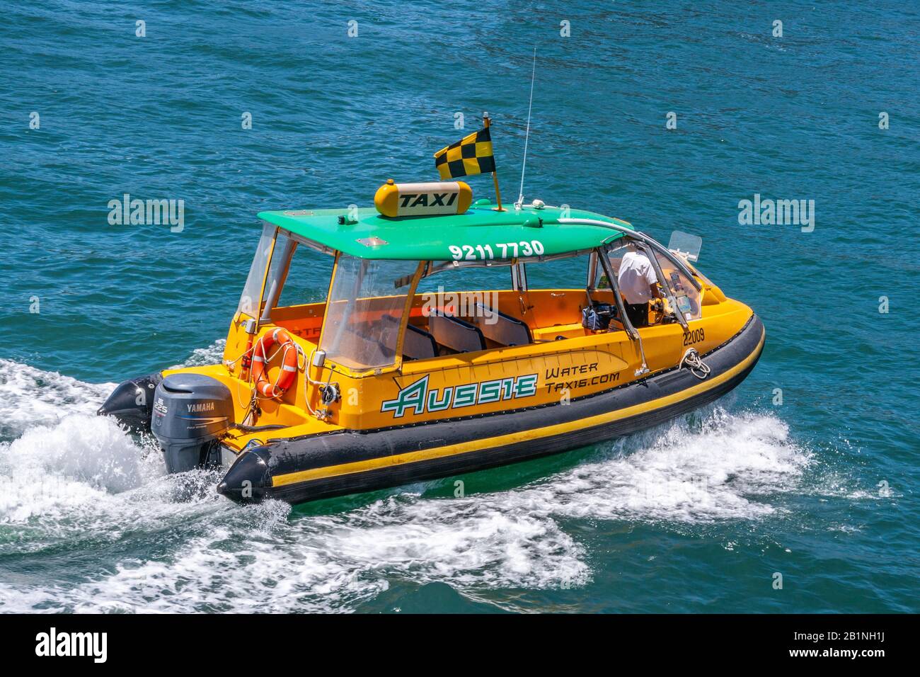 Sydney, Australia - December 11, 2009: Closeup of small deep-yellow and green water-taxi on blue bay water producing white surf behind. Stock Photo