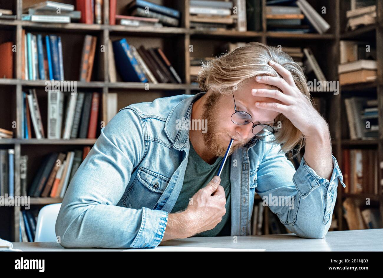 Serious smart focused student glasses library desk think on task solve problem. Stock Photo
