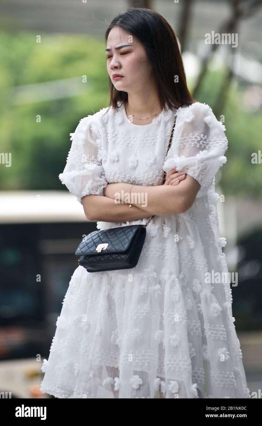 Wuhan: A young woman with a white dress and a black purse waiting at the exit of Chuhe Hanije metro station, Zhong Bei Lu street. China Stock Photo