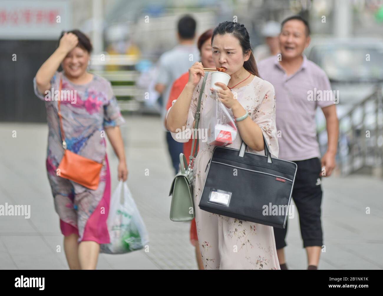 Wuhan: Chinese woman eating with chopsticks while walking down the street at the exit of Chuhe Hanije metro station, Zhong Bei Lu street. China Stock Photo