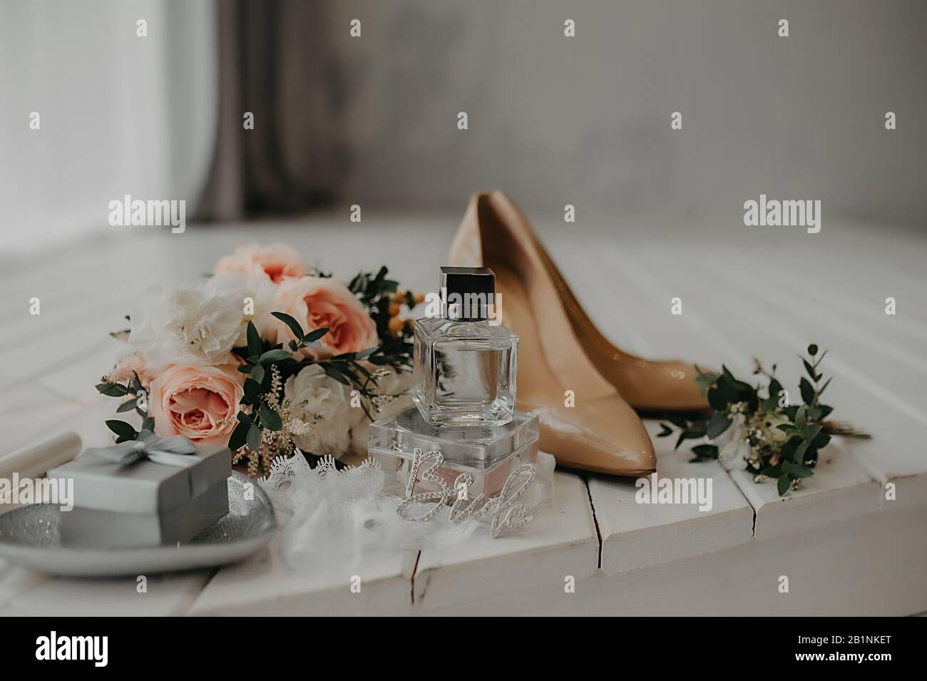 accessories for the bride who dresses up for the wedding: beige patent leather shoes, perfume and a cute stylish bouquet of small roses in a light int Stock Photo