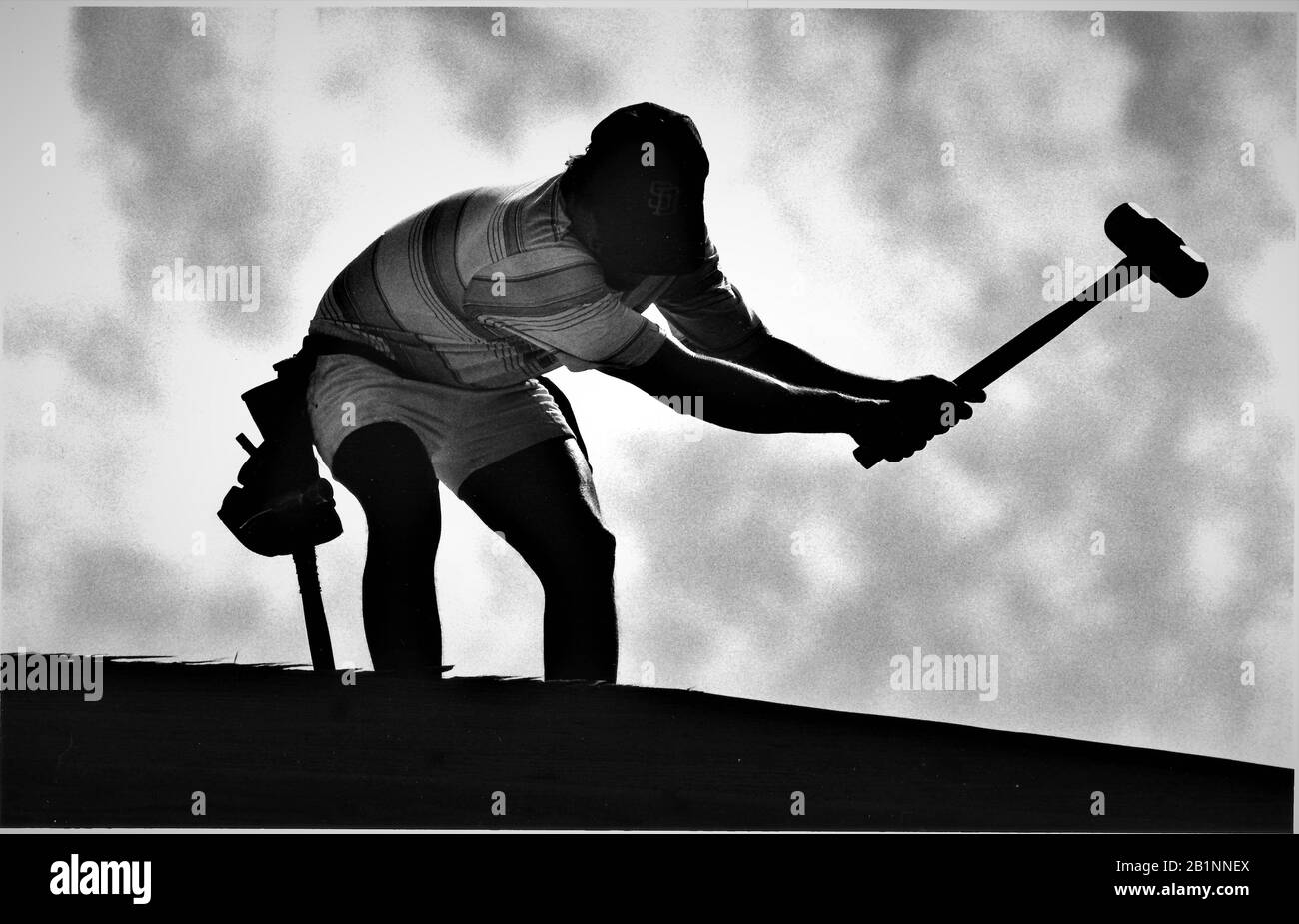 Young man working on taking down removal of older building for make space to rebuild silhouette with sledgehammer and tool belt on roof Stock Photo