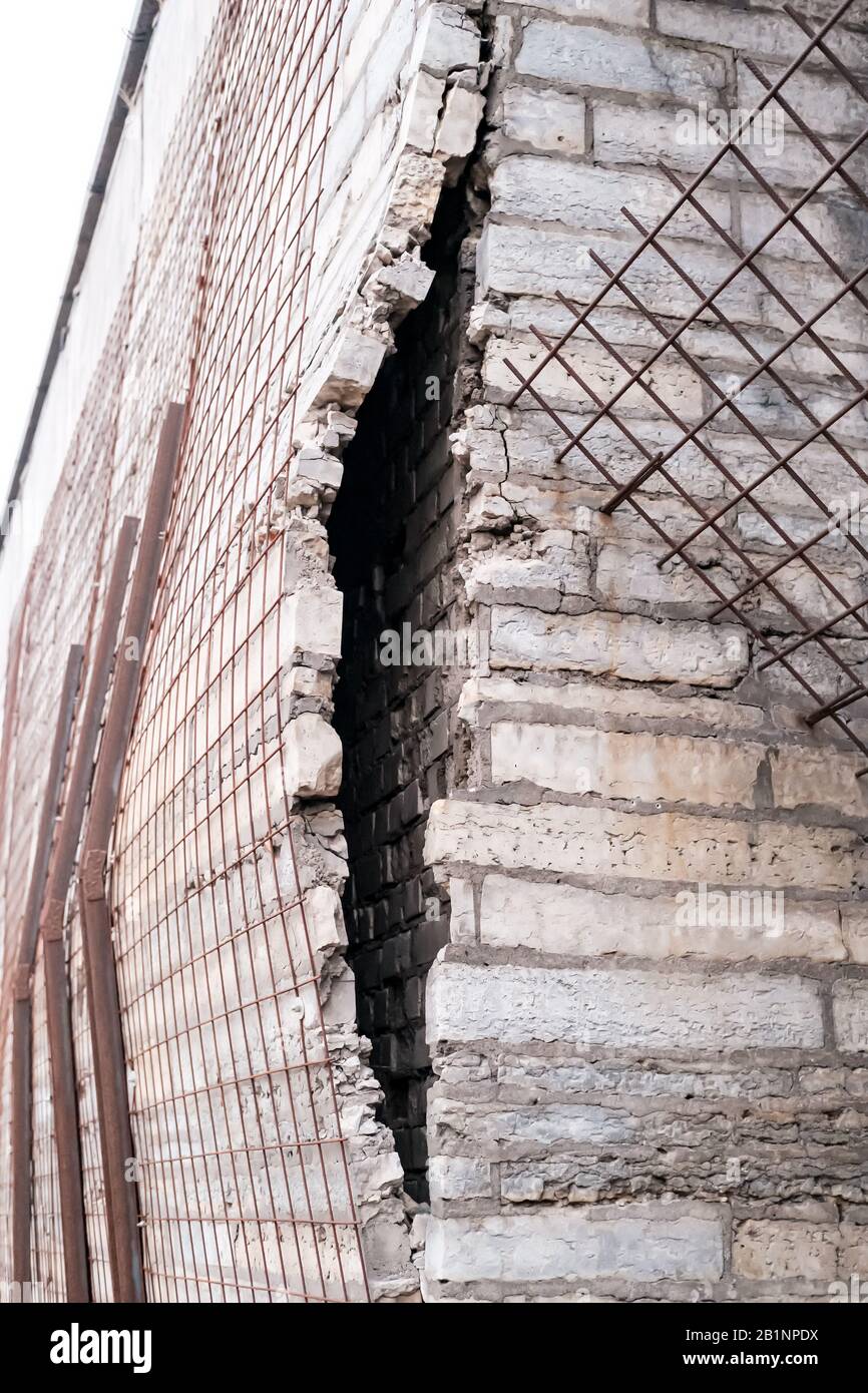 Stone cladding falls off from the brick wall of the building and is held back by metal pipes and mesh. Stock Photo