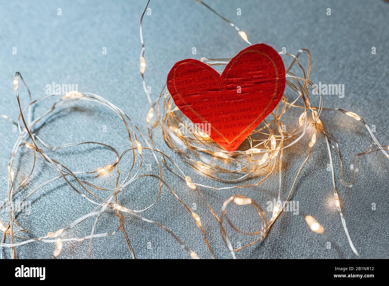 bright red eco-friendly heart made of paper wrapped in garlands and bulbs on a blue uniform background, postcard for a loved one about love and feelin Stock Photo