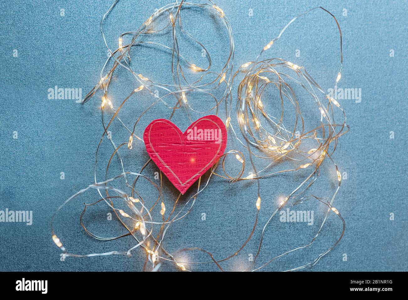 bright red eco-friendly heart made of paper wrapped in garlands and bulbs on a blue uniform background, postcard for a loved one about love and feelin Stock Photo