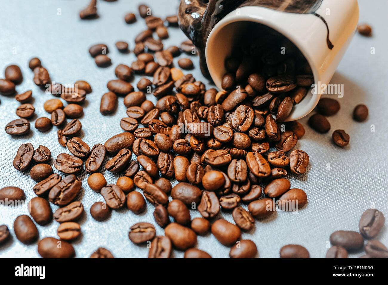 ready-made picture for coffee advertising and ready for publication, a large number of coffee roasted beans are scattered around a white mug full of b Stock Photo