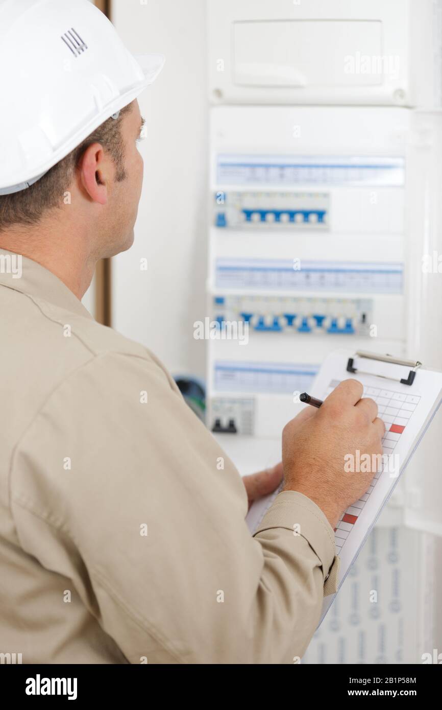 electrician worker checking clipboard while working in fuse-board Stock Photo