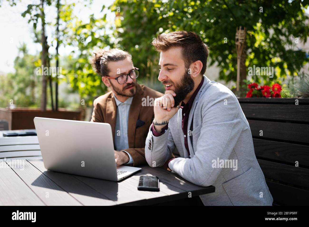 Positive successful business specialists discussing plan with laptop outdoors. Stock Photo