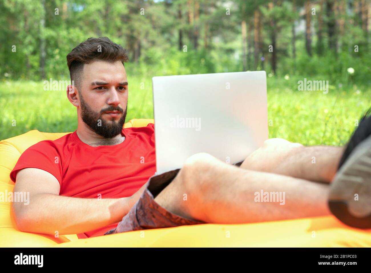 Workaholic man working on laptop during vacation, remote work. Freelancer in nature background Stock Photo