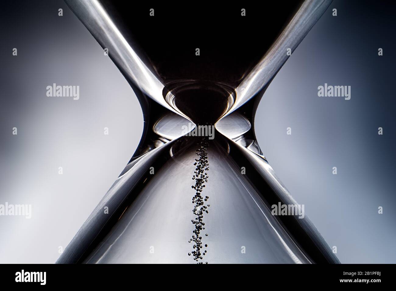 Minimalist close up of hourglass with black sand and light coming from behind, reflection on surface Stock Photo