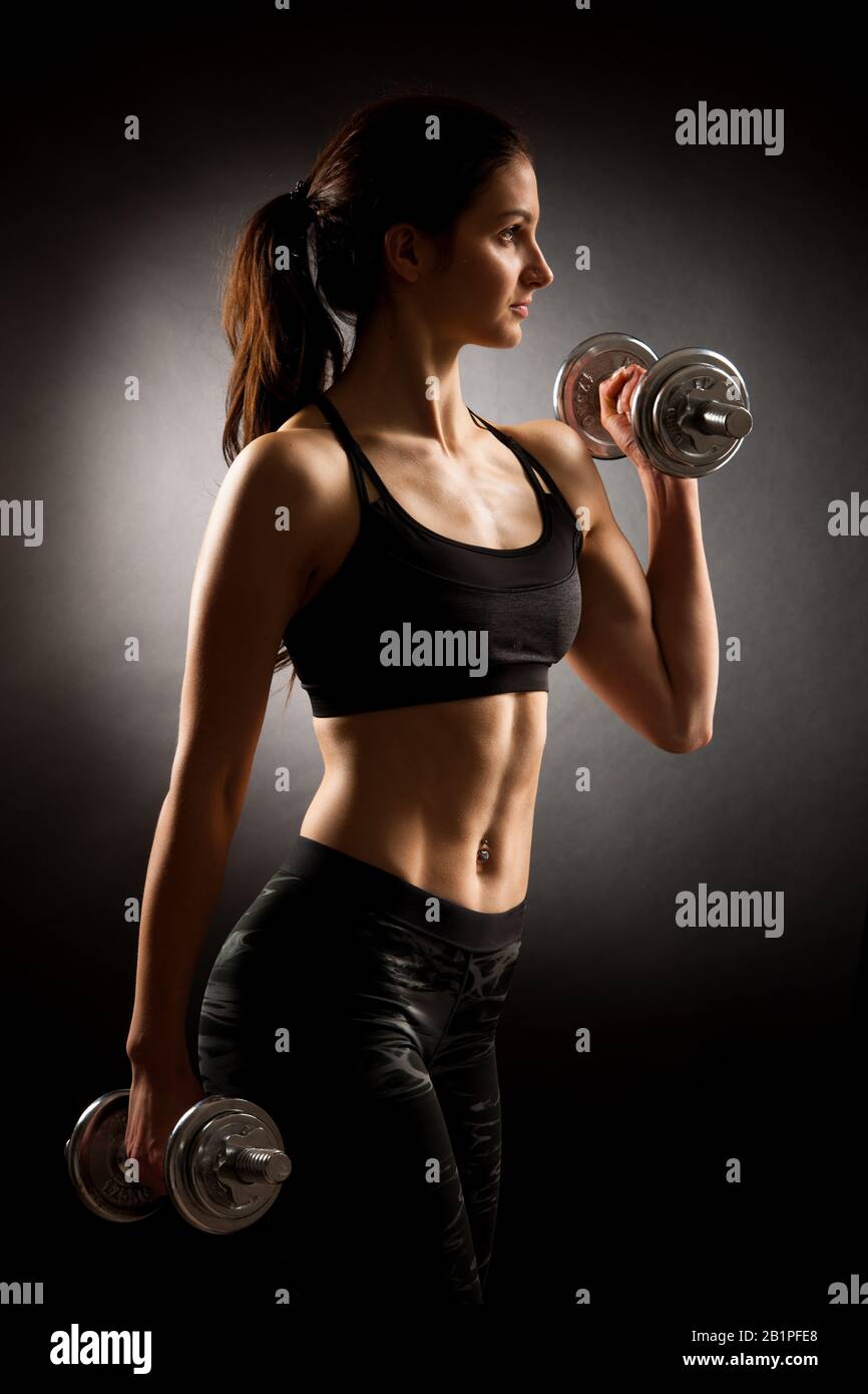 Atractive fit woman works out with dumbbells as a fitness conceptual over dark background. Stock Photo