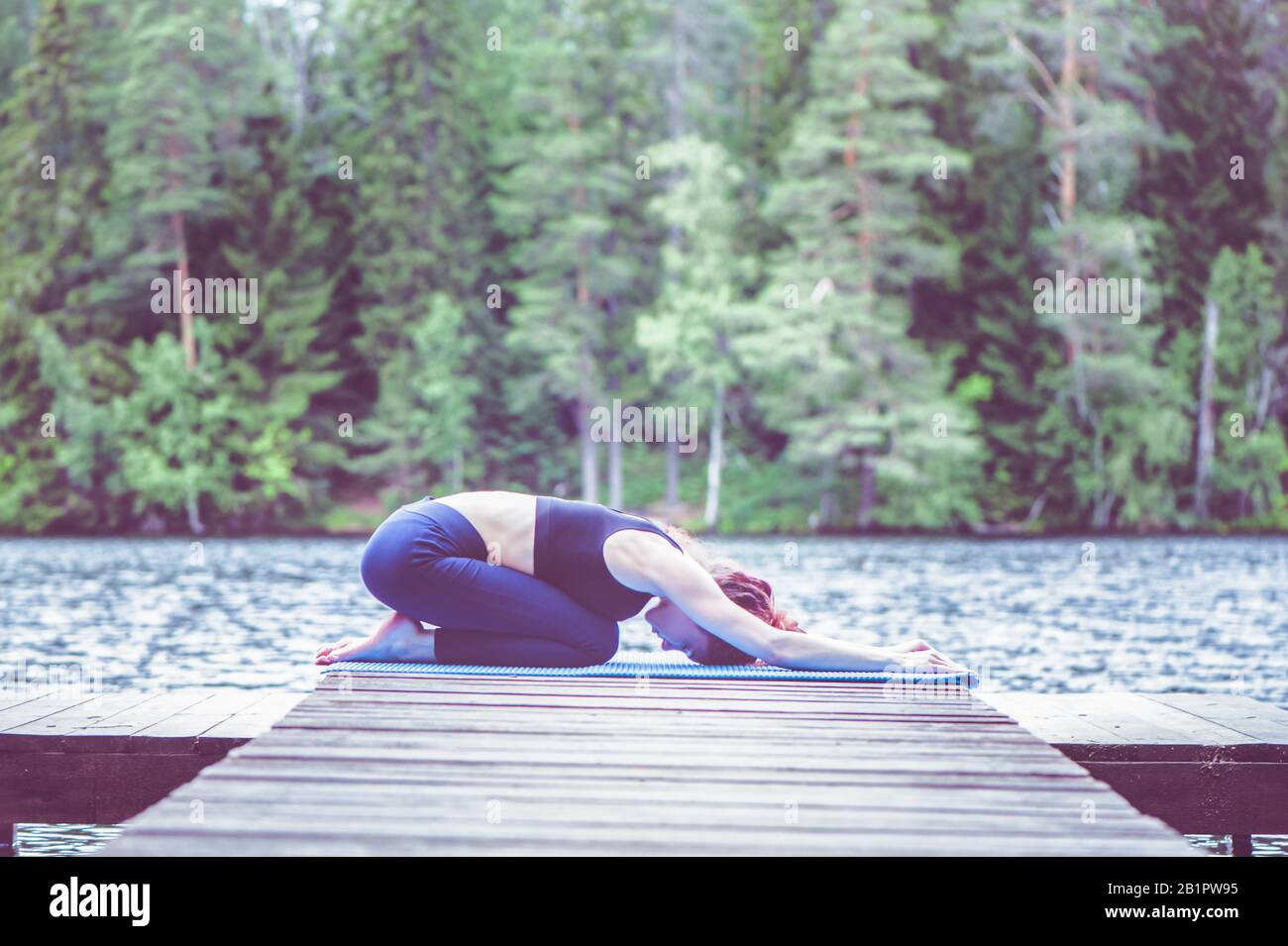 Young attractive girl practicing yoga, sitting in Child exercise, Balasana pose  on the lake. The concept of appeasement,  healthy lifestyle Stock Photo