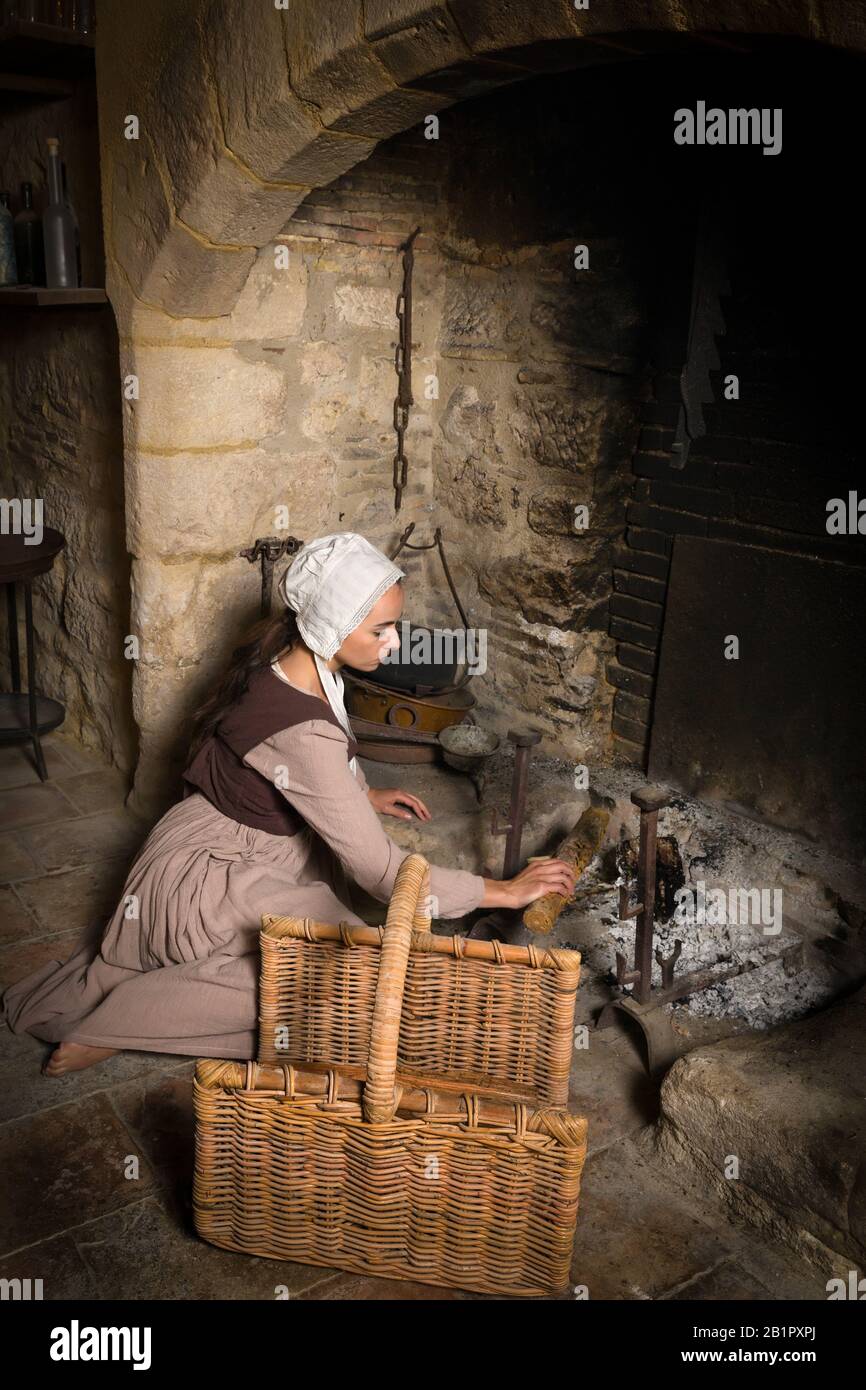 Renaissance portrait in Rembrandt style of a young woman in medieval peasant costume working near the authentic fireplace of a property released Frenc Stock Photo
