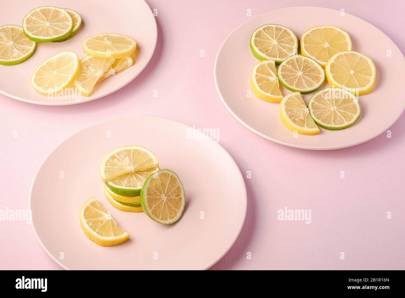 Fresh tasty lemon and lime citrus fruits slices on three pink plates, minimal background isolated, angle view Stock Photo